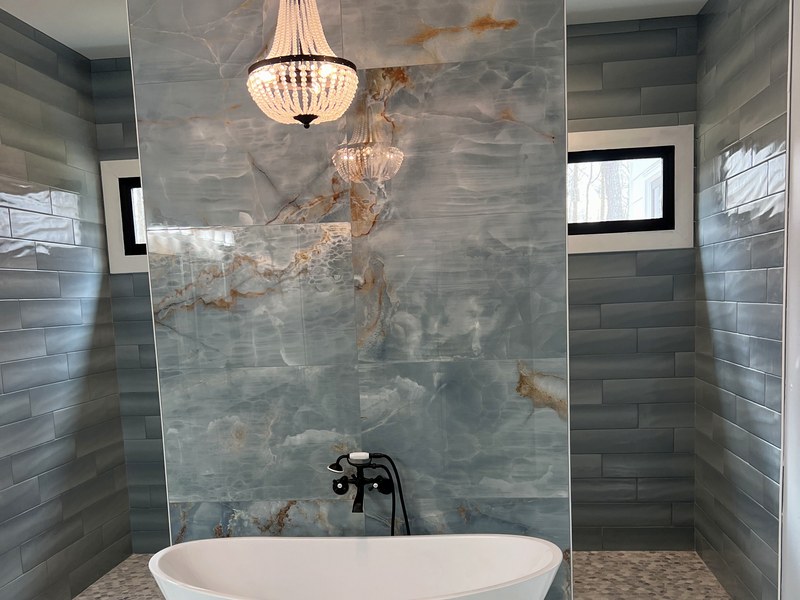 Master bath with a backlit onyx-look porcelain feature wall, a freestanding soaking tub, and a hand-beaded chandelier: a RYMAC custom build in Canton, GA.