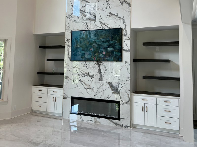 Two-story fireplace wall in large-format marble-look porcelain with custom built-ins and floating shelves: a RYMAC custom build in Suwanee, GA.