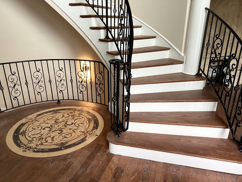 Curved staircase with custom-forged ironwork, stained-wood treads, and an inlaid wood floor medallion: a RYMAC custom home in Gainesville, GA.