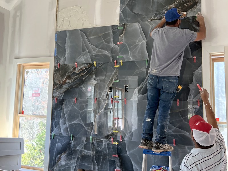 Two tile setters hand-leveling an onyx-look porcelain feature wall mid-install: a RYMAC jobsite craft shot.